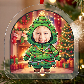 Personalized Christmas tree ornament in clear acrylic — a real photo face on a cute cartoon Christmas-tree onesie with baubles and lights, on a red ribbon
