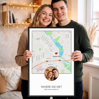 Couple holding a framed personalized Where We Met map print — a Boise, Idaho street map with a red heart marker and their photo, in a black frame.