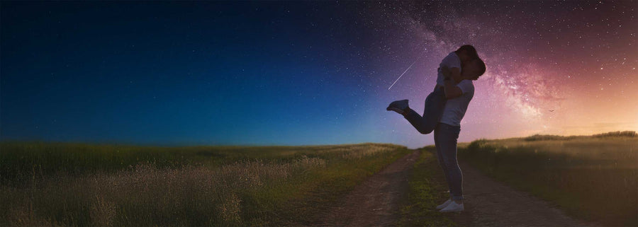 Romantic couple embracing under a starry night sky with the Milky Way visible above a country road at sunset