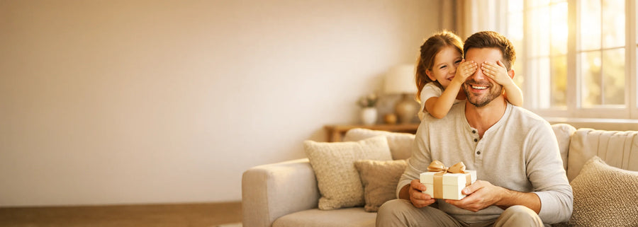 Man and child sitting on a couch with a cup, smiling indoors.