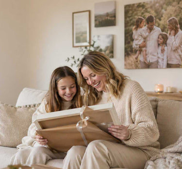 Woman and young girl sitting on a couch, looking at a photo album together.