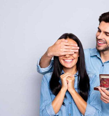 Man surprising smiling woman with custom jewelry box gift featuring a personalized message card. (M)